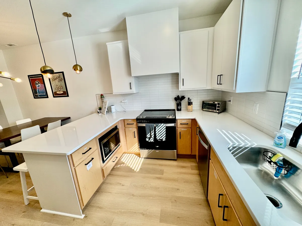 This image highlights a spacious, contemporary kitchen with a central island, stainless steel appliances, and sleek modern cabinetry. The adjacent dining area is visible, reinforcing the centrality of communal meals and gatherings. The overall mood is warm and welcoming, perfect for both casual and celebratory occasions.