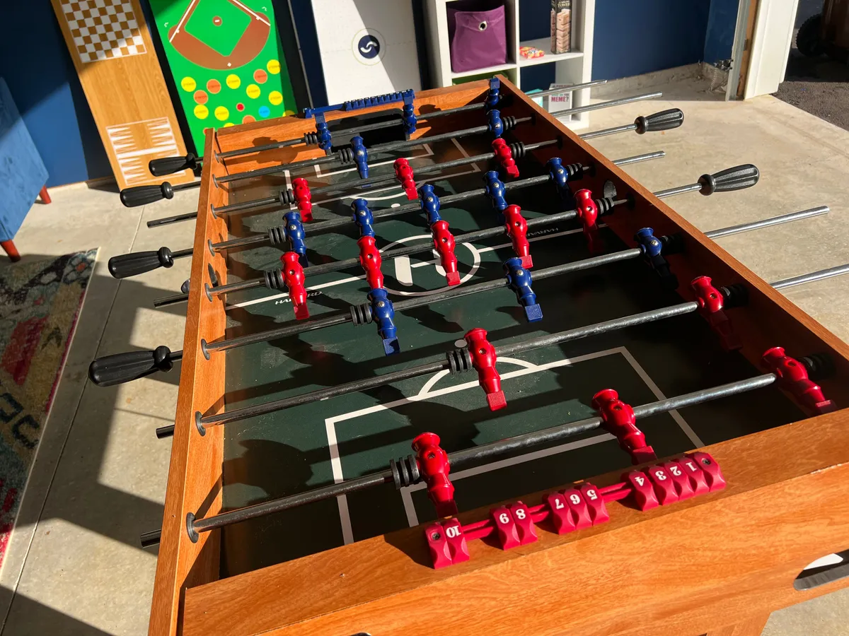 An energetic interior view of a foosball table in a dedicated game room, with colorful player figures and a visible scoreboard. The mood is lively and playful, suggesting a perfect spot for friendly competition and post-night-out fun.