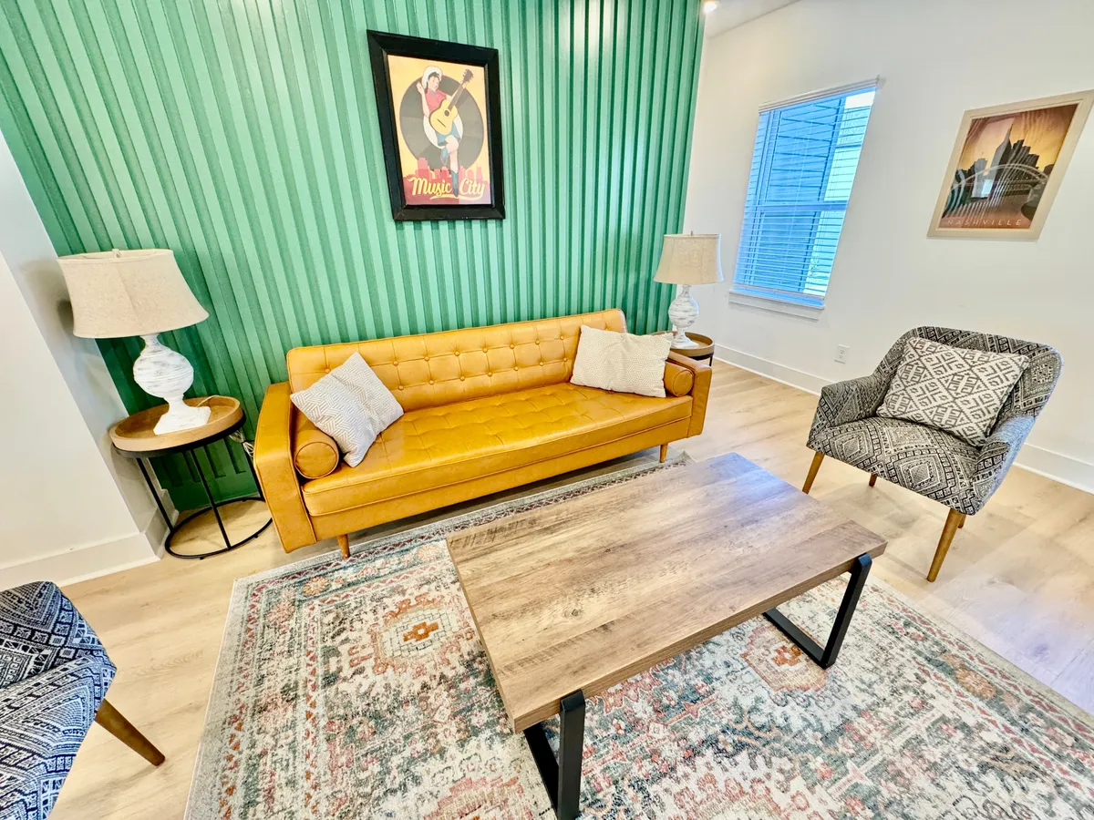 A cheerful living space adorned with a yellow sofa, green accent wall, wooden coffee table, decorative rug, and artwork. The ambiance is vibrant and perfect for socializing or enjoying a quiet moment with friends or family.
